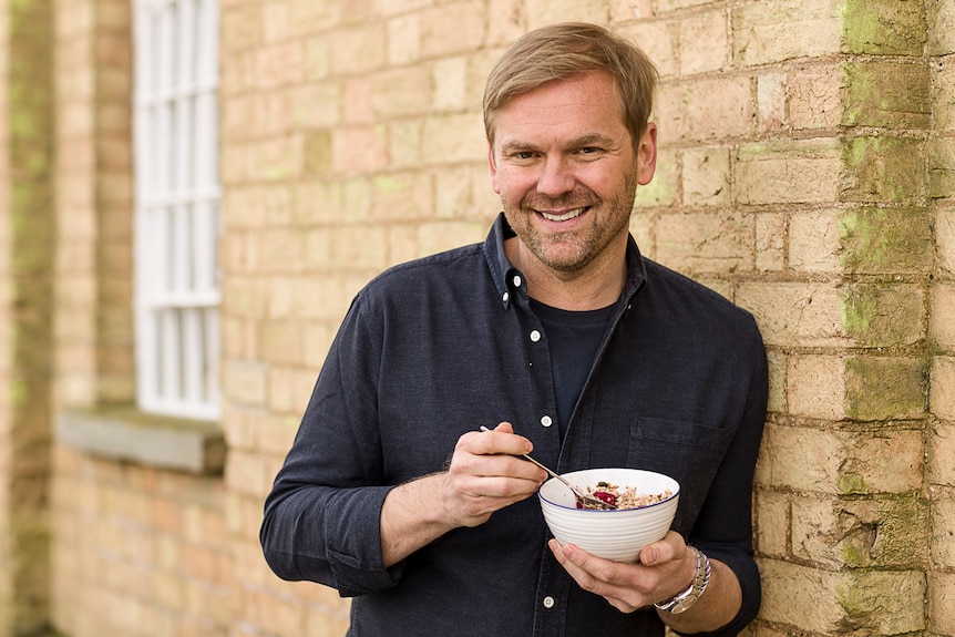 Celebrity chef Bill Granger holds a bowl of muesli and leans against a brick wall