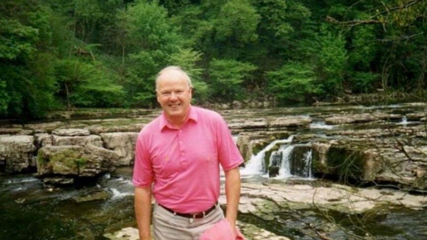 Man in pink shirt standing in front of a lake/river