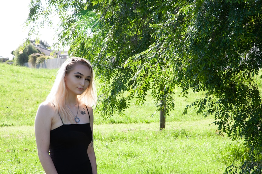 A woman stands in a field next to a tree