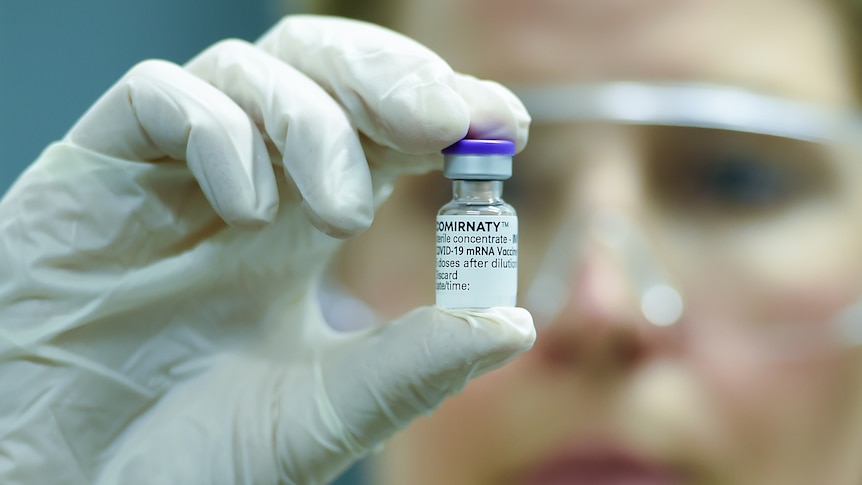 a woman wearing protective goggles holding onto a vial of vaccine dose