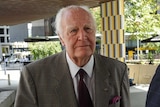 Peter Hollingworth, dressed in a suit, walks towards a building in a CBD environment.