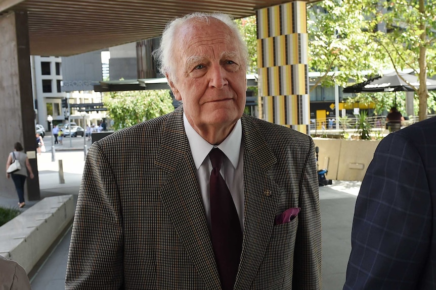 Peter Hollingworth, dressed in a suit, walks towards a building in a CBD environment.