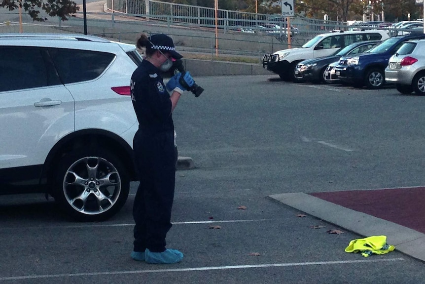 A police forensics officer films a yellow item of police clothing on the ground outside an East Perth stationery shop.