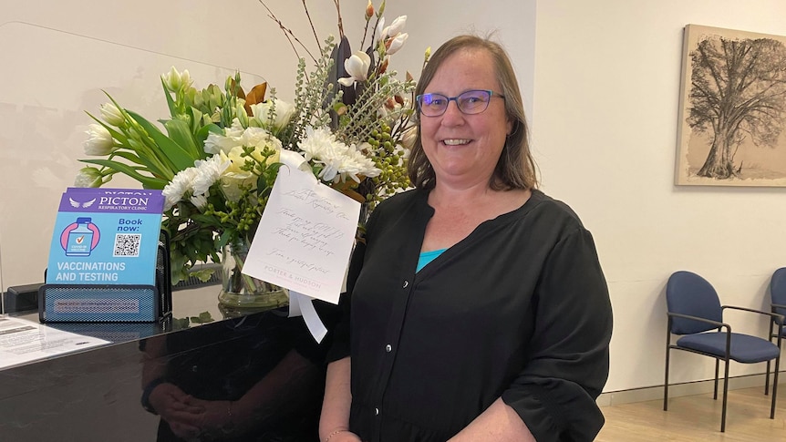 A woman stands next to a big bunch of flowers