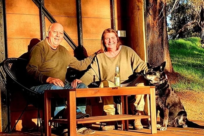 A man and a woman sit at a table with a dog