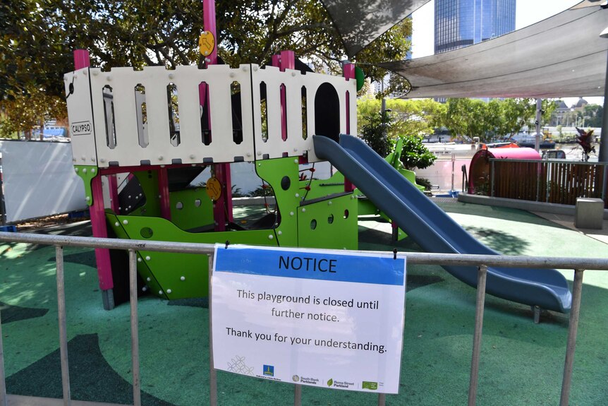 A sign is taped to a playground fence saying the equipment is closed until further notice