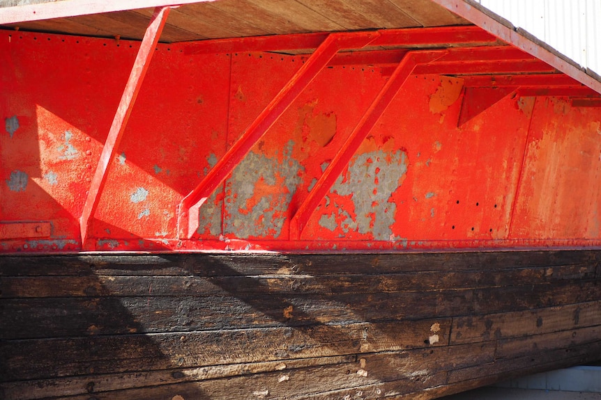 A weathered-looking barge with a rusty and peeling red hull.