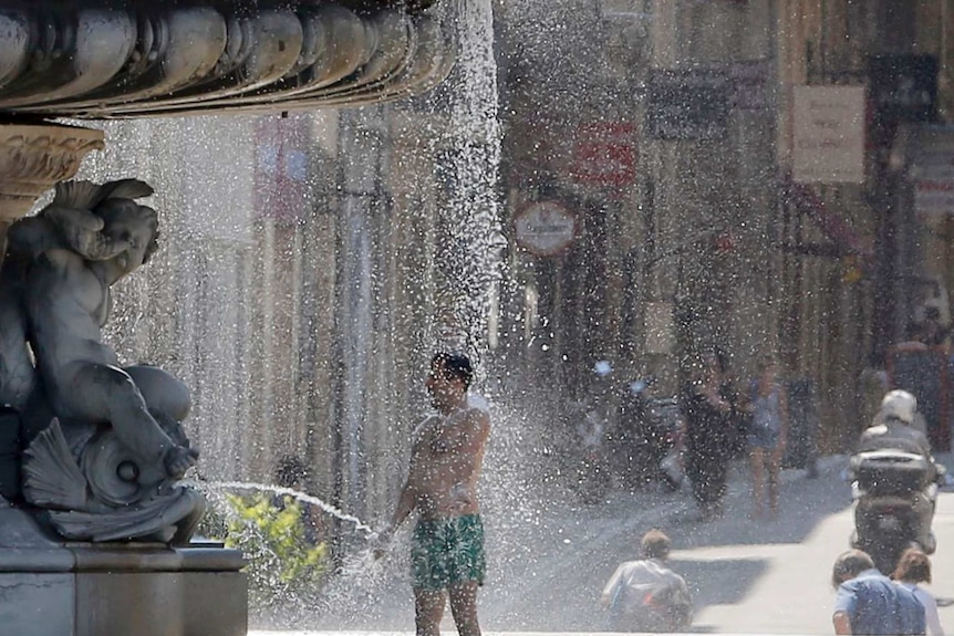 A man cools off in a fountain during a warm summer day in Bordeaux