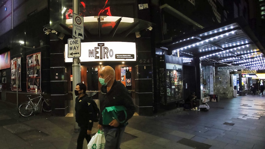 people in masks walking past a closed theatre at night