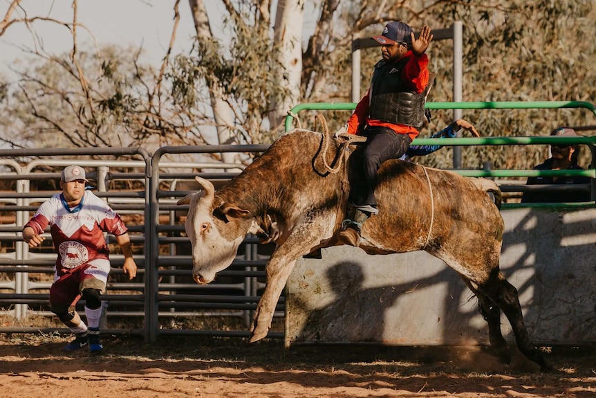 Man in red shirt riding bucking bull.