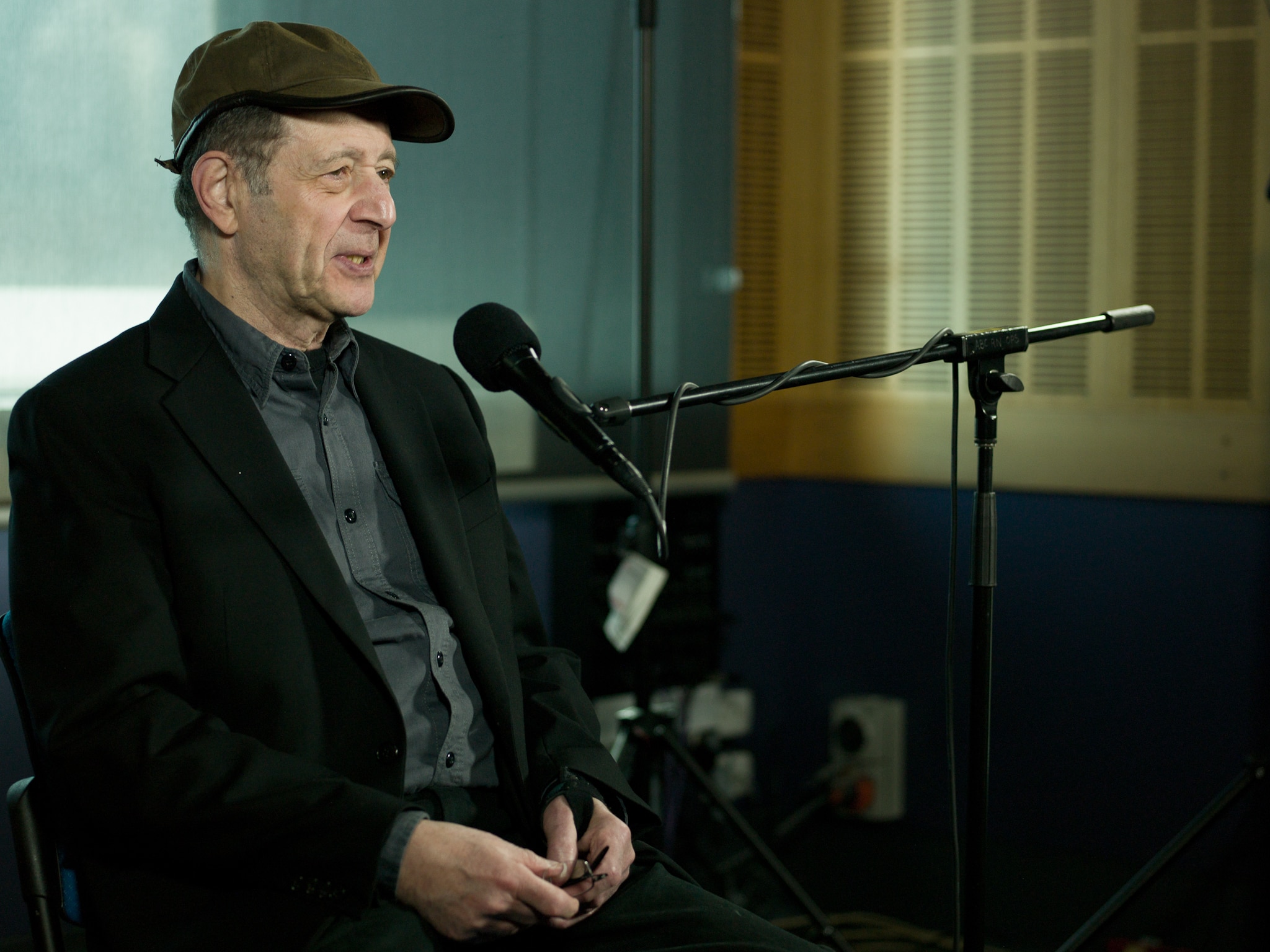 Steve Reich in a cap and blazer sitting behind a guest microphone in the Radio National studios.