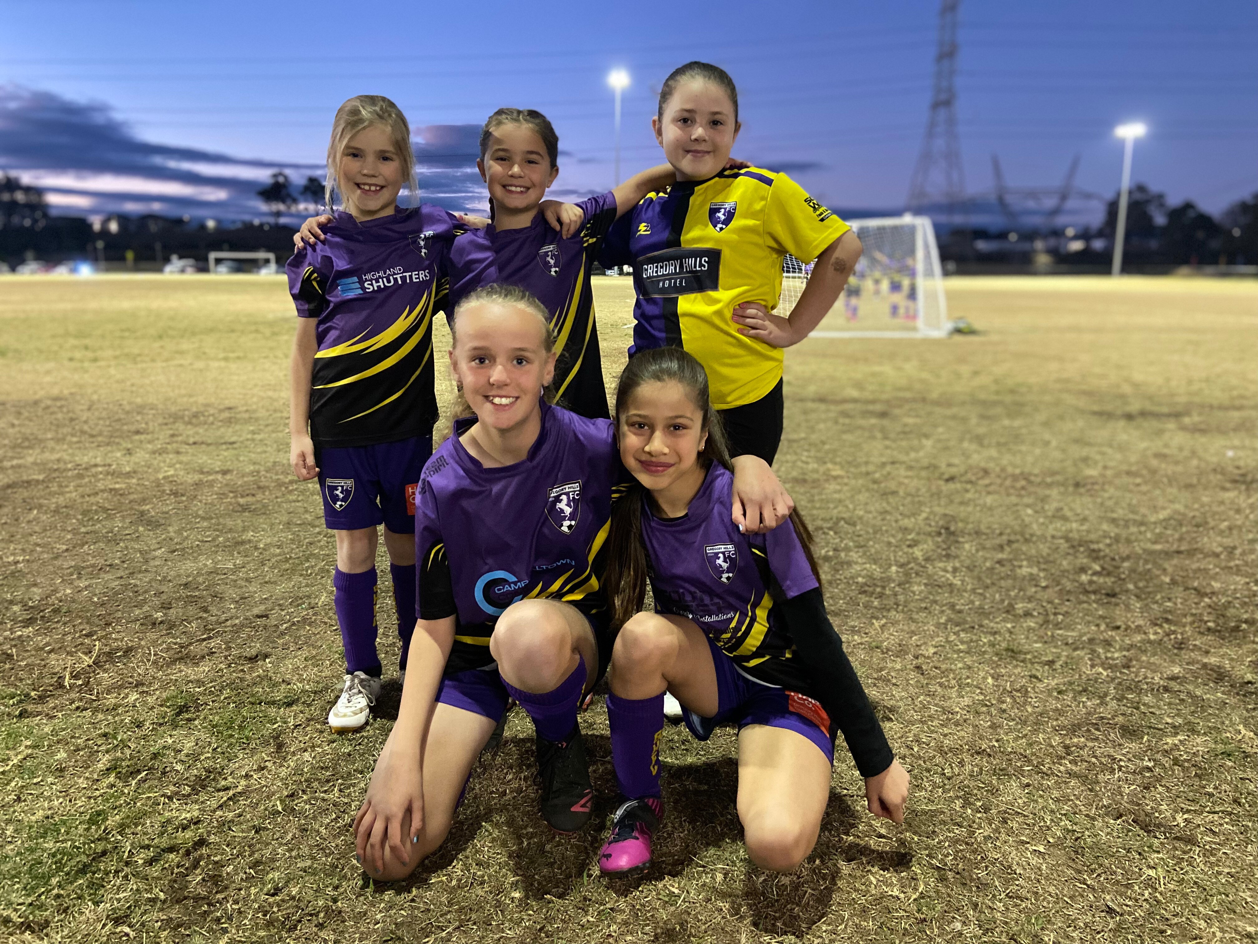 five young girl soccer players in uniform on a soccer field
