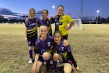 five young girl soccer players in uniform on a soccer field