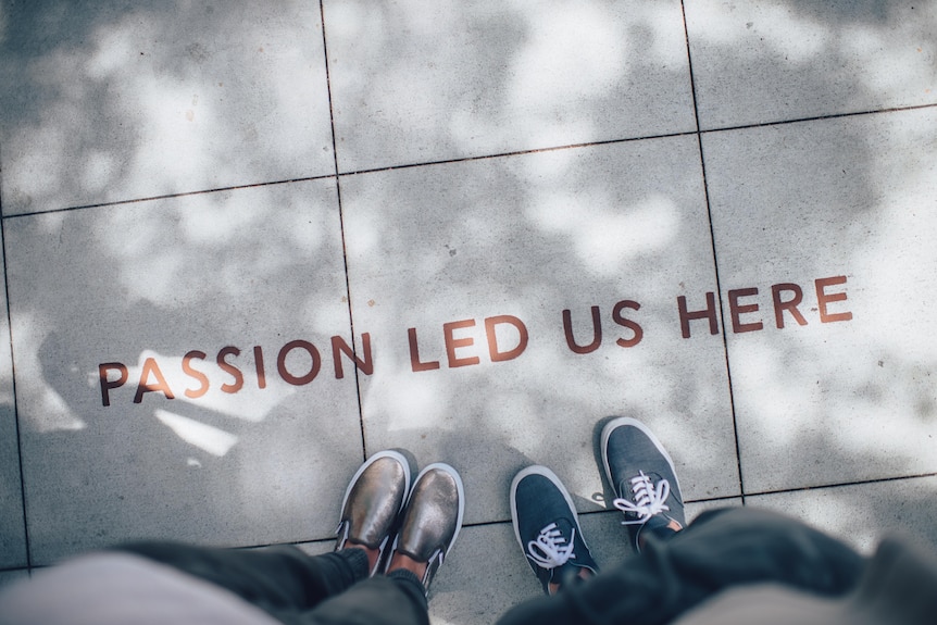 Bird's eye view of two people's feet and the word passion written in the pavement.