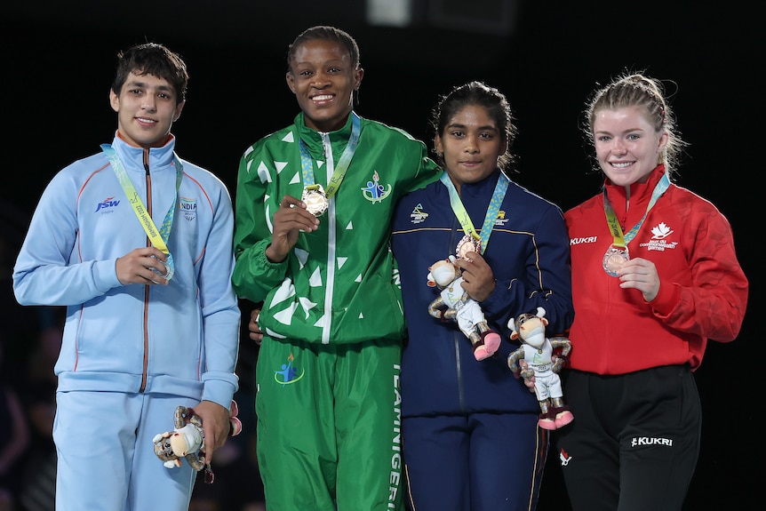 Four women wrestlers stand on a podium with medals around their necks.