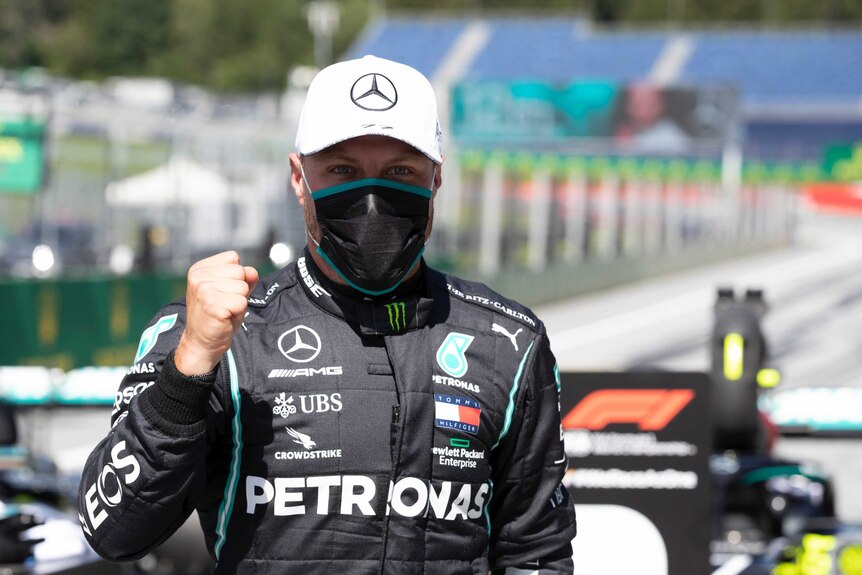 Valtteri Bottas stands with a clenched fist wearing a black facemask and white cap