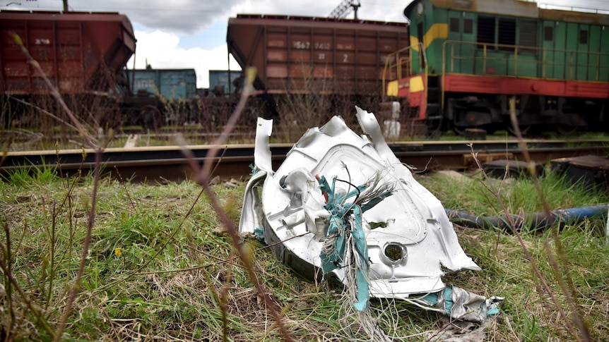 Metal debris lies on the ground in front of trains.