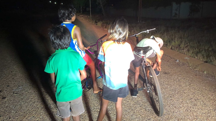 A photo of four children playing on their bikes in the street at night.