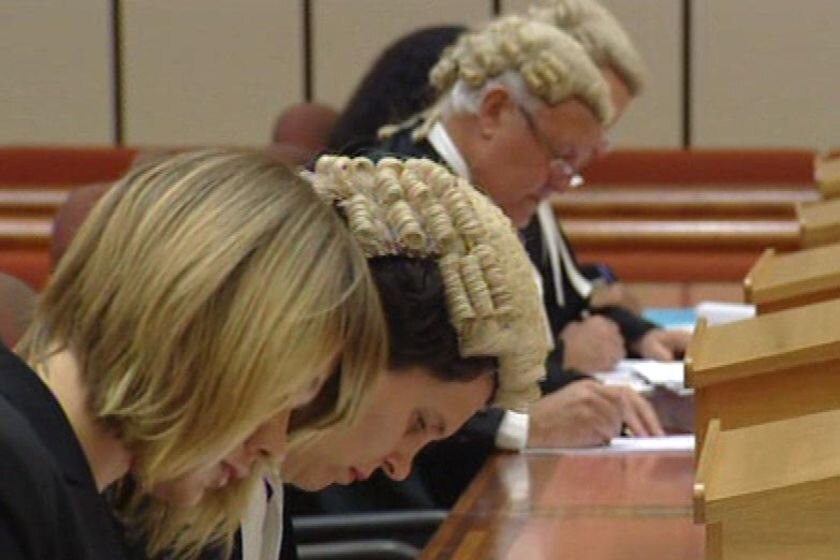 Generic TV still of close-up of row of barristers and lawyers writing in a court room bench