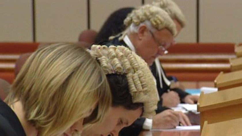Generic TV still of close-up of row of barristers and lawyers writing in a court room bench