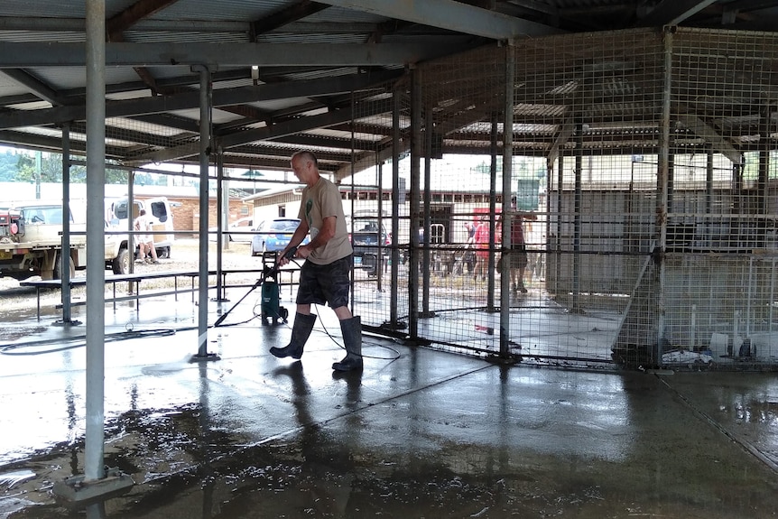 A man hoses mud out of a shed.