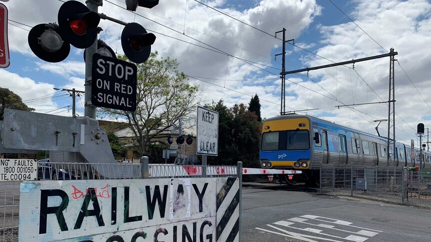A train moves across a closed level crossing with red warning lights and boom gates down.