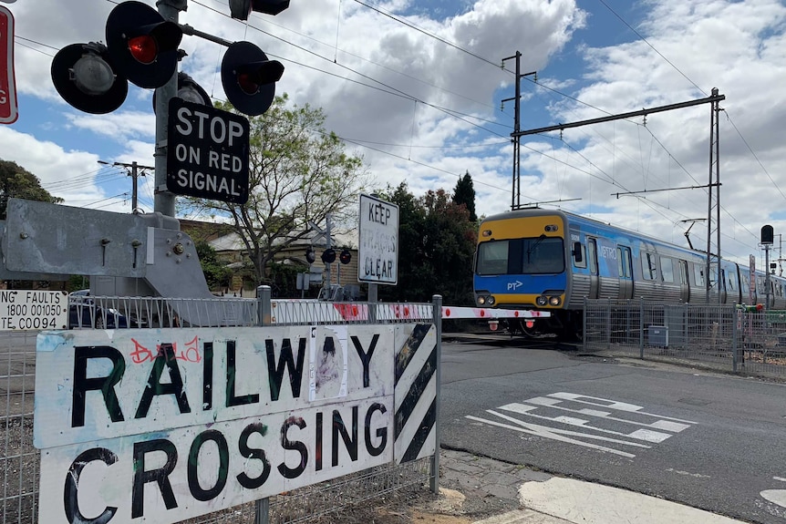 A train moves across a closed level crossing with red warning lights and boom gates down.