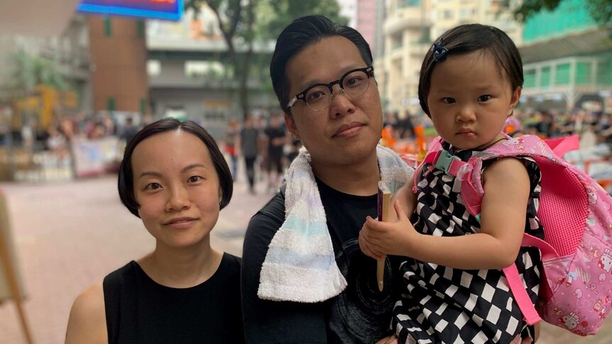 A couple pose for a photo with their daughter on the street