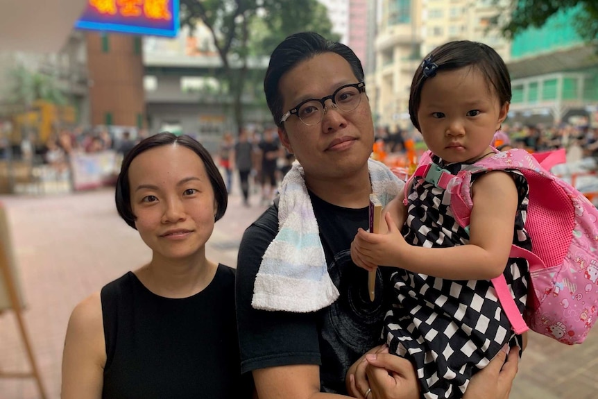 A couple pose for a photo with their daughter on the street