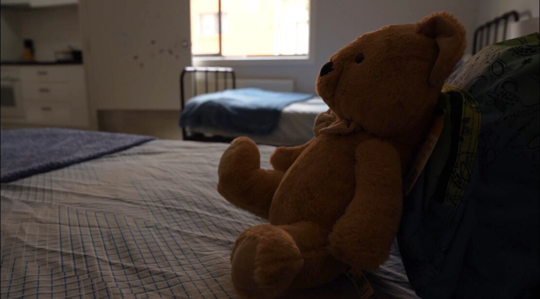 A teddy bears sits on a bed.
