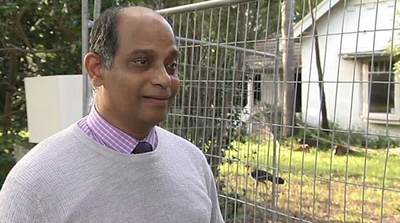 A man standing in front of a fence which has a bush turkey behind it.