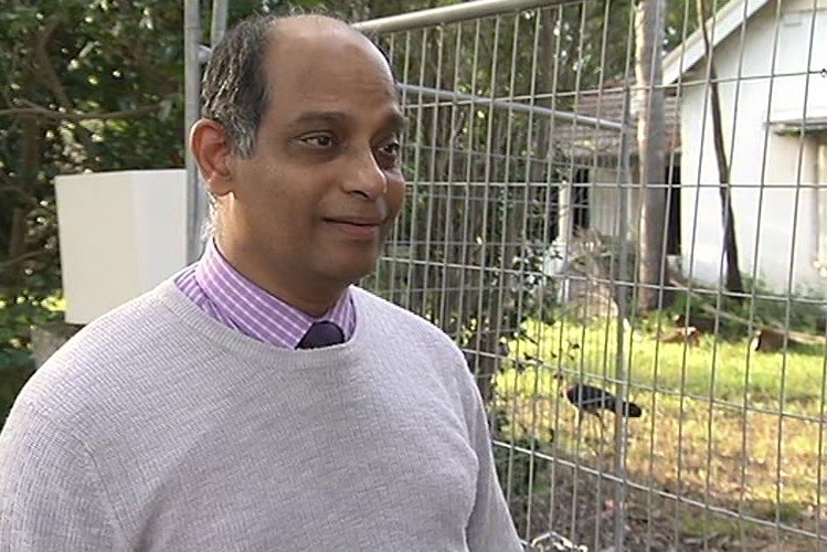 A man standing in front of a fence which has a bush turkey behind it.