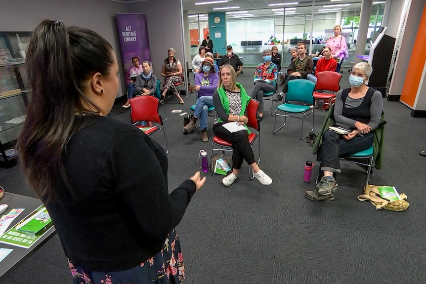 Women speaking to a group of people indoors. 