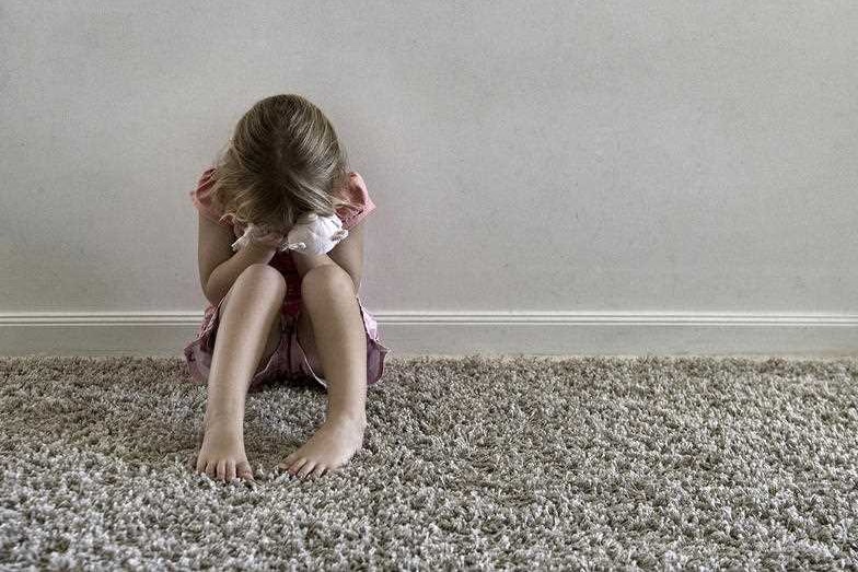 A stock image of a child hiding, looking upset.
