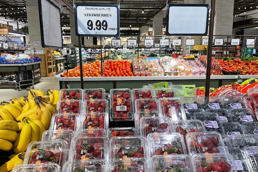 Punnets of strawberries sit on a store display with a price card above stating $9.99 for a 250g punnet. 
