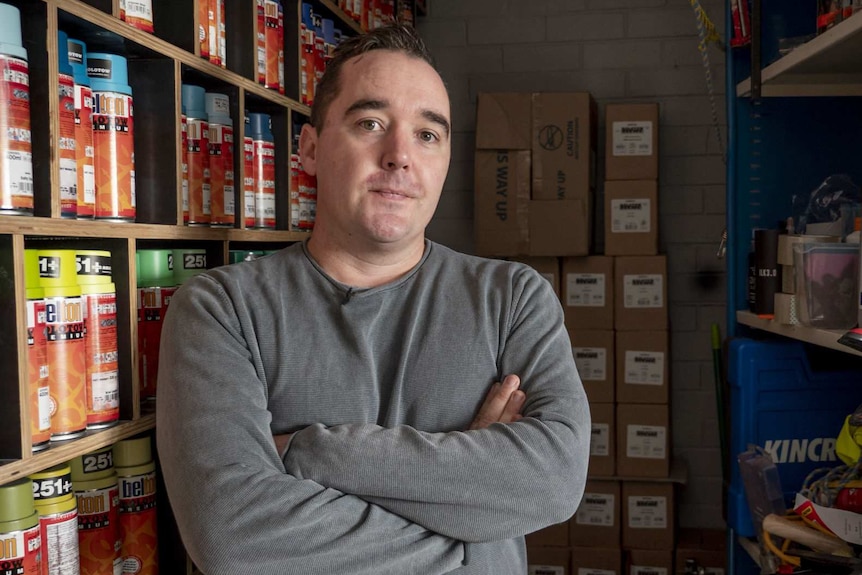 Artist Luke Cornish standing in front of shelves of spray paint.