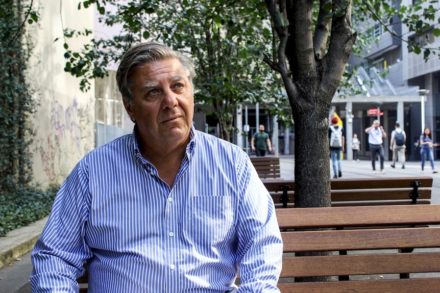 Tony sits on a bench under a tree looking at the sky.