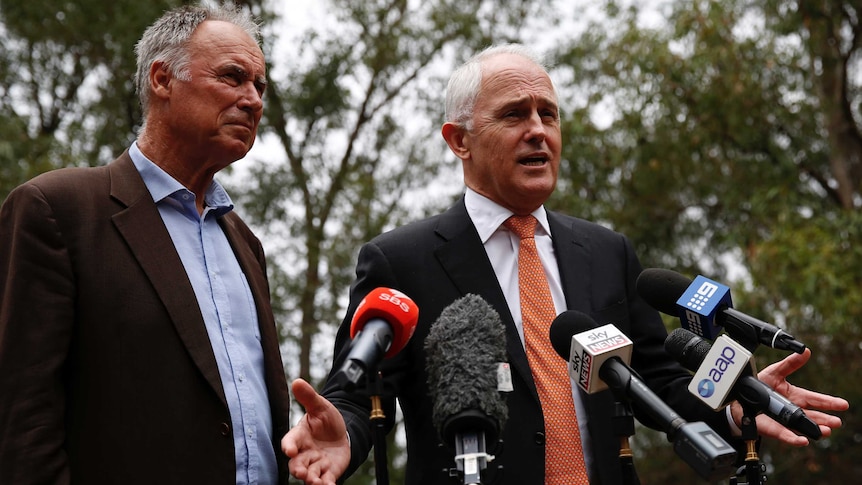 Malcolm Turnbull gestures as he speaks into microphones. John Alexander watches on beside him.