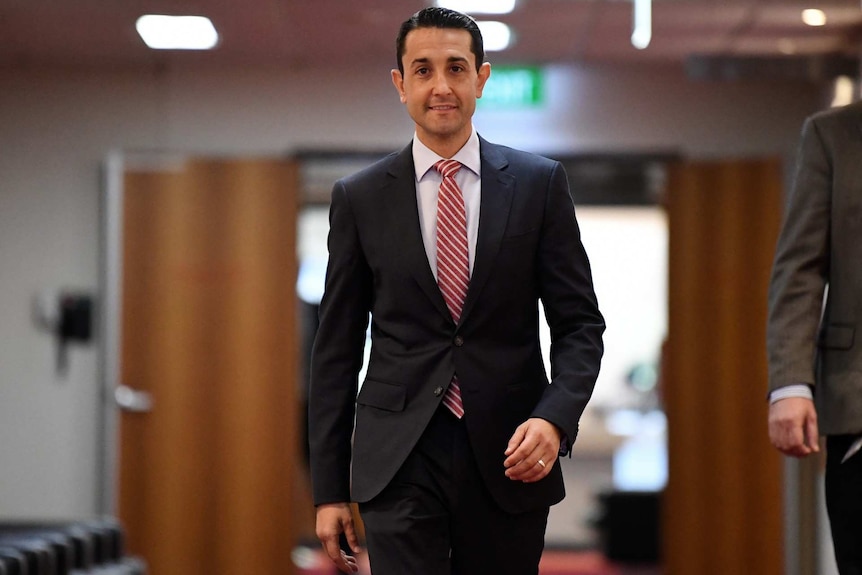 Man in dark suit wearing a red striped tie walks down a corridor