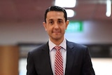 Man in dark suit wearing a red striped tie walks down a corridor