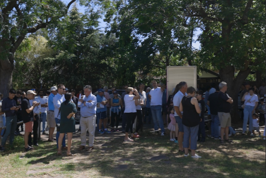 A group of people huddle around the front yard of a property during an auction