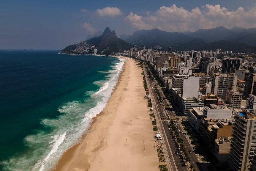An aerial view of a beautiful beach with buildings beside and mountain in background.