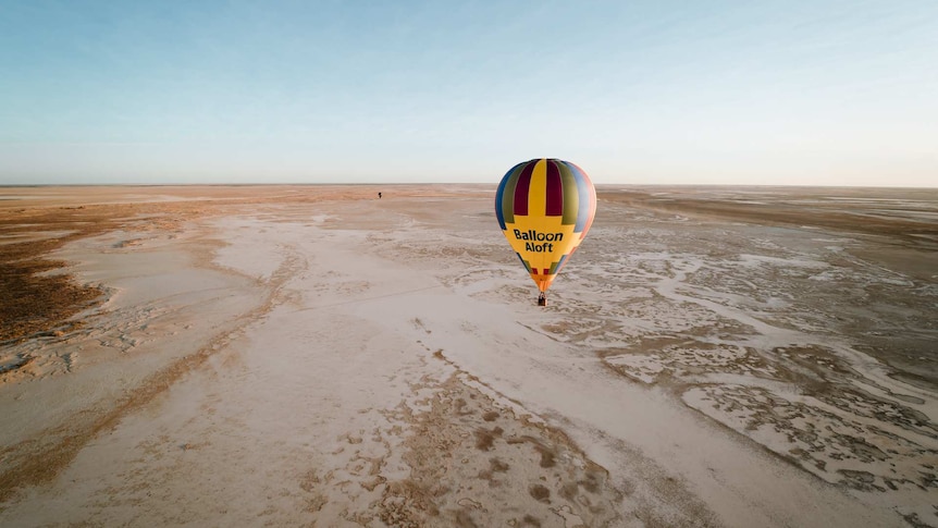 A yellow and multicoloured hot air balloon mid flight over saltpans.