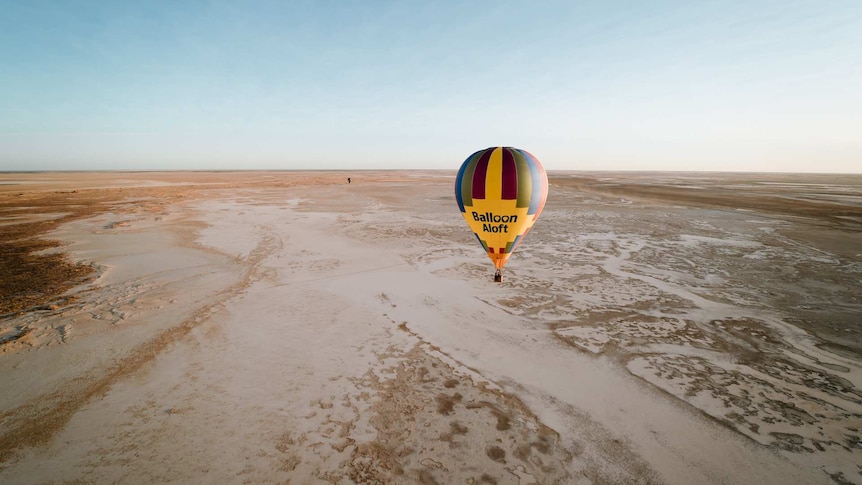 A yellow and multicoloured hot air balloon mid flight over saltpans.