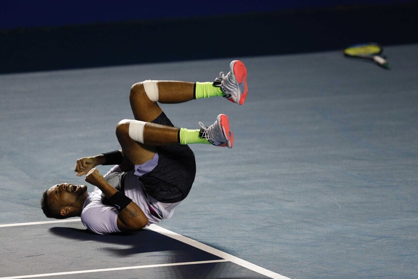 Nick Kyrgios lies on his back on the court screaming in joy.