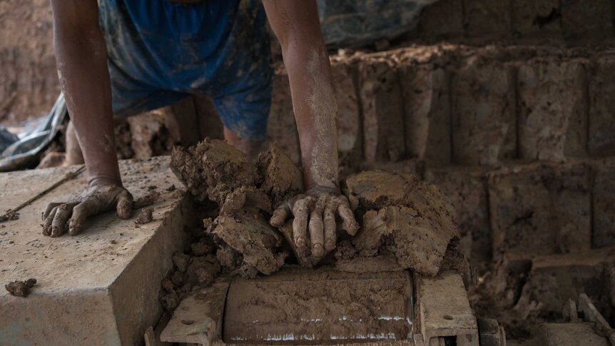 A man feeds clay into a brick-moulding machine in Cambodia.