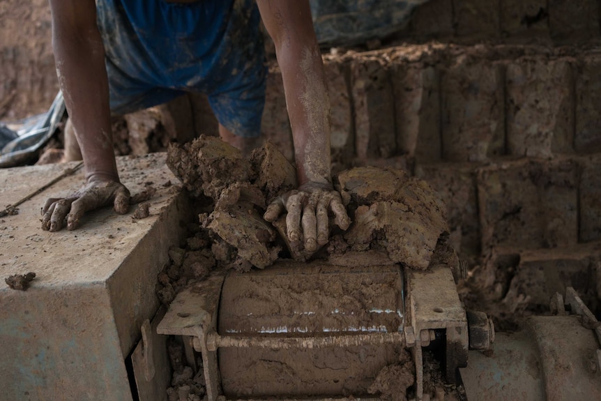 A man feeds clay into a brick-moulding machine in Cambodia.