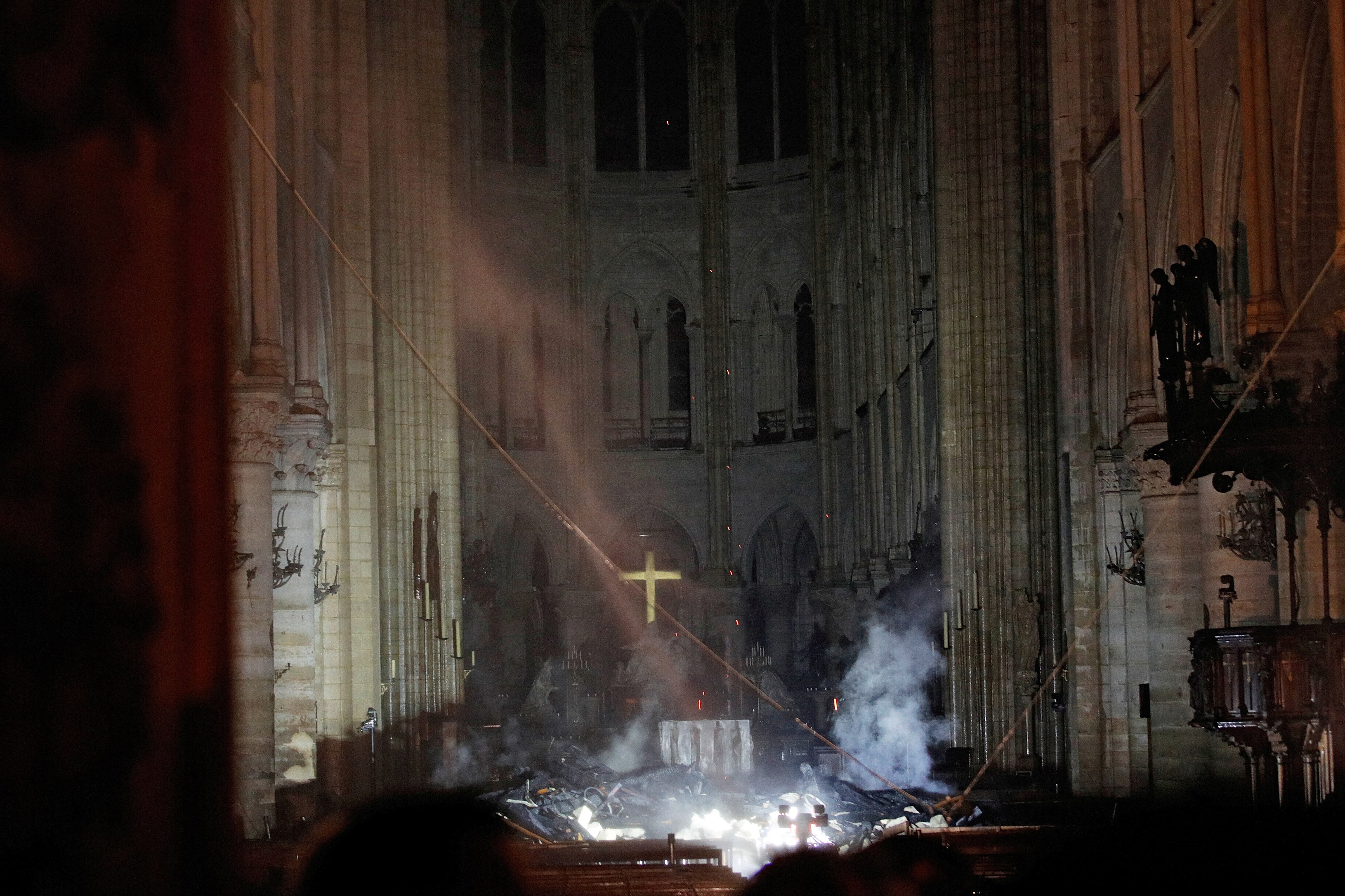 The smoking inside of an eerily burnt church with a golden cross visible behind rubble