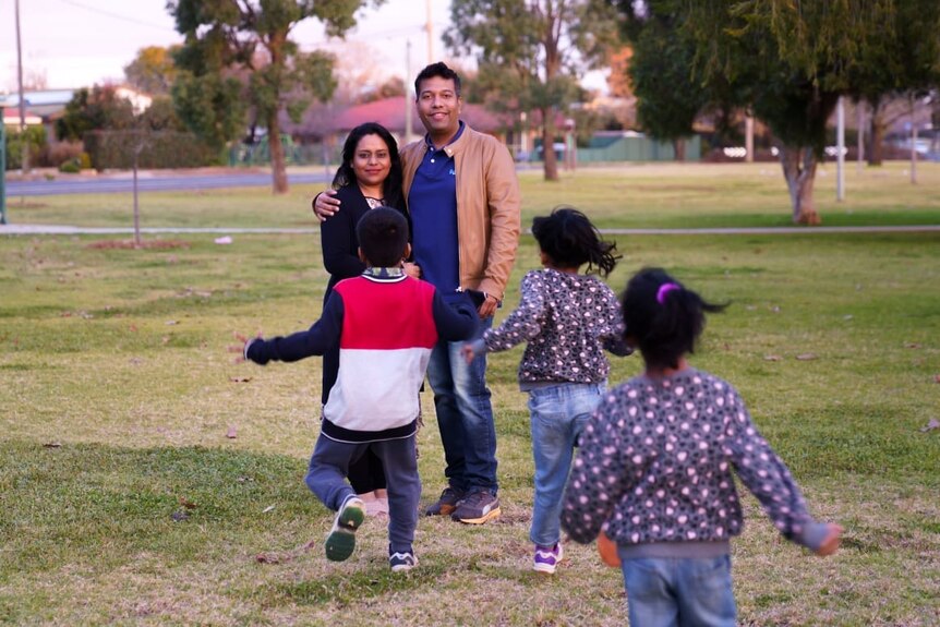 A man his wife smile at the camera while three children run towards them