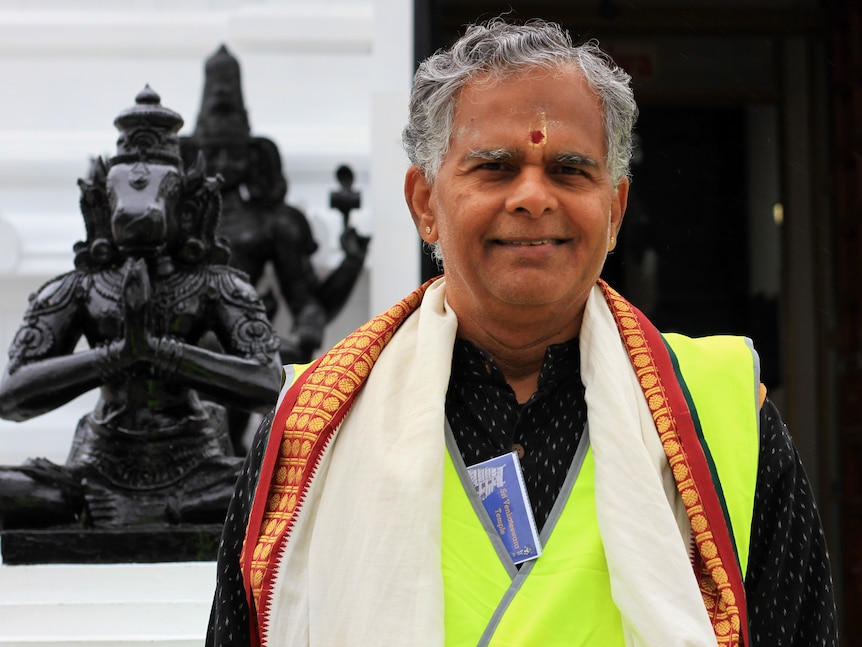 Man stands in front of temple wearing robes